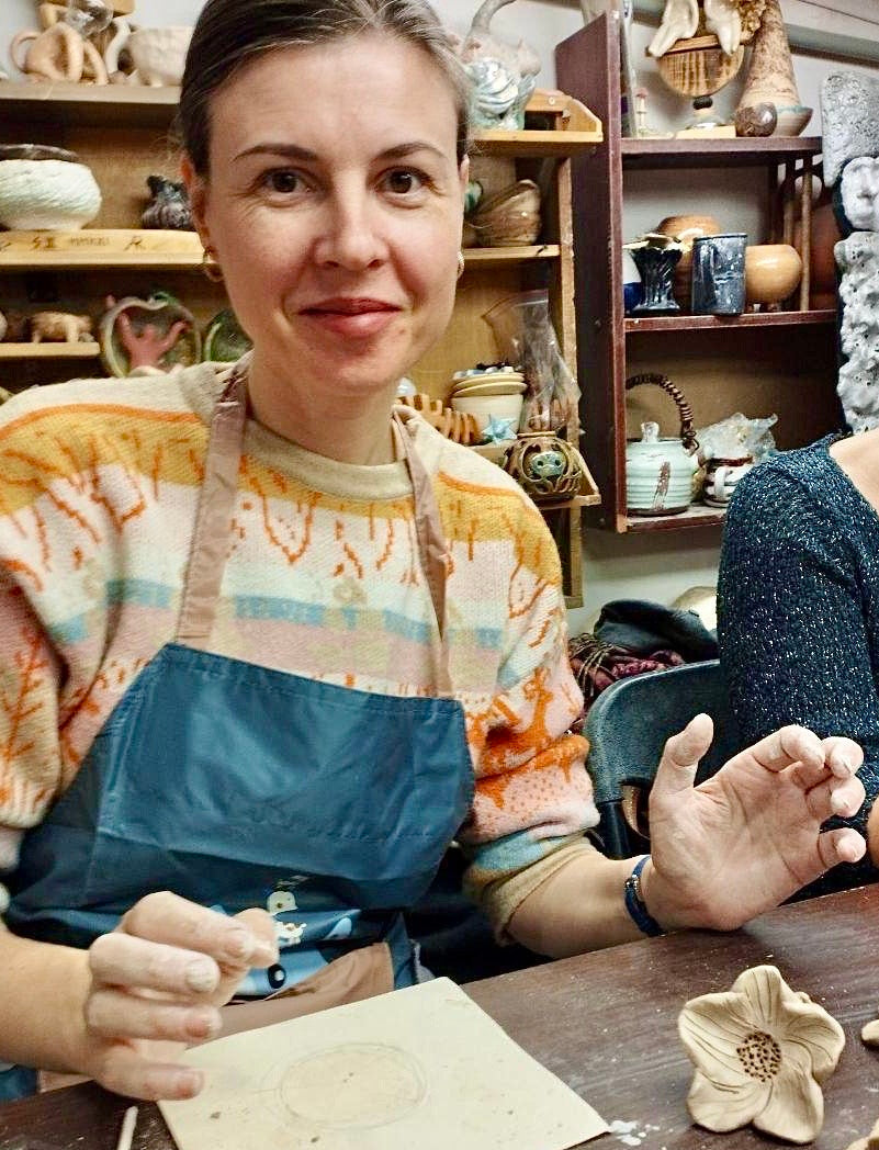 Ukrainian woman in a pottery studio with ceramic items and tools on a table.