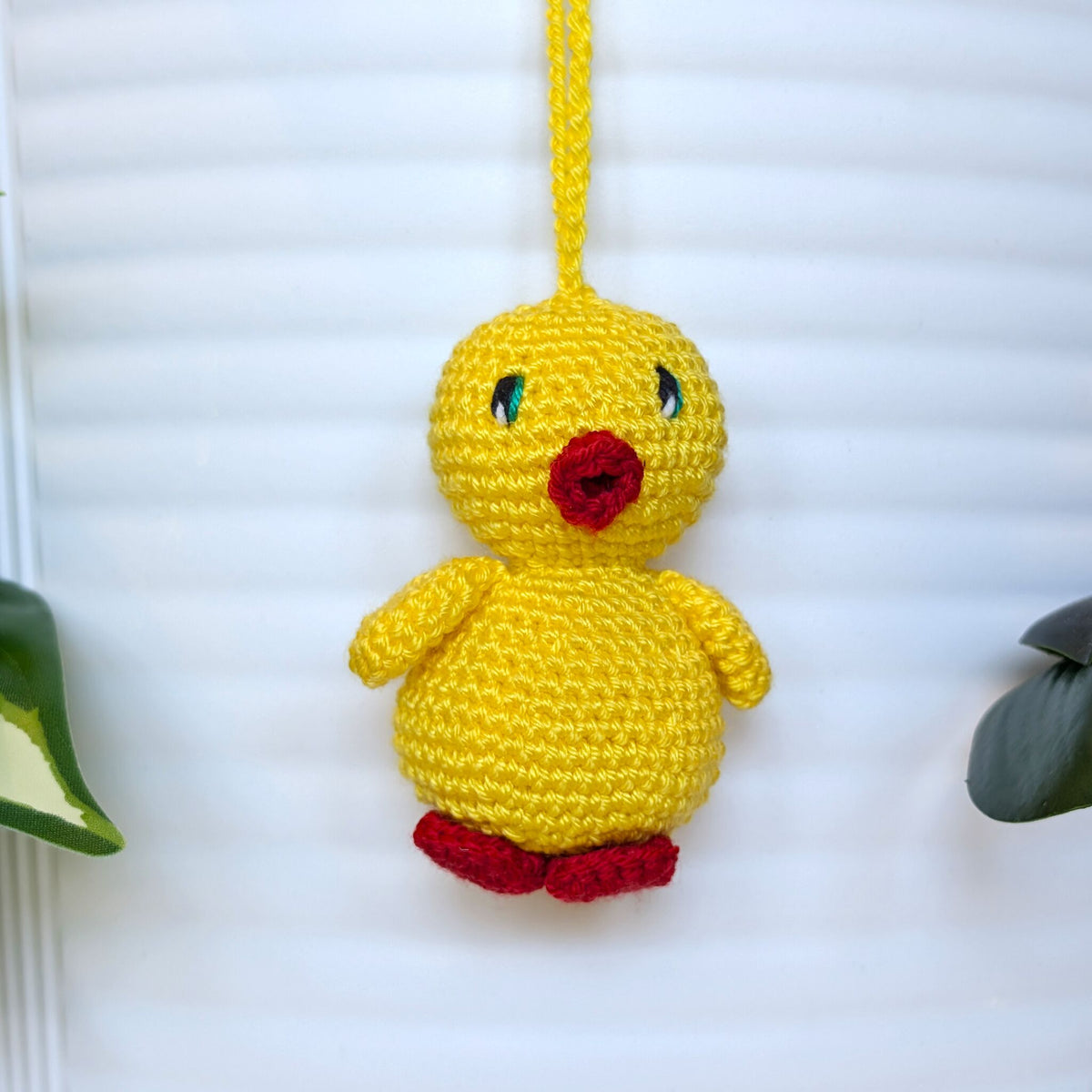 Crocheted yellow chick with jade green eyes, red beak and feet attached string