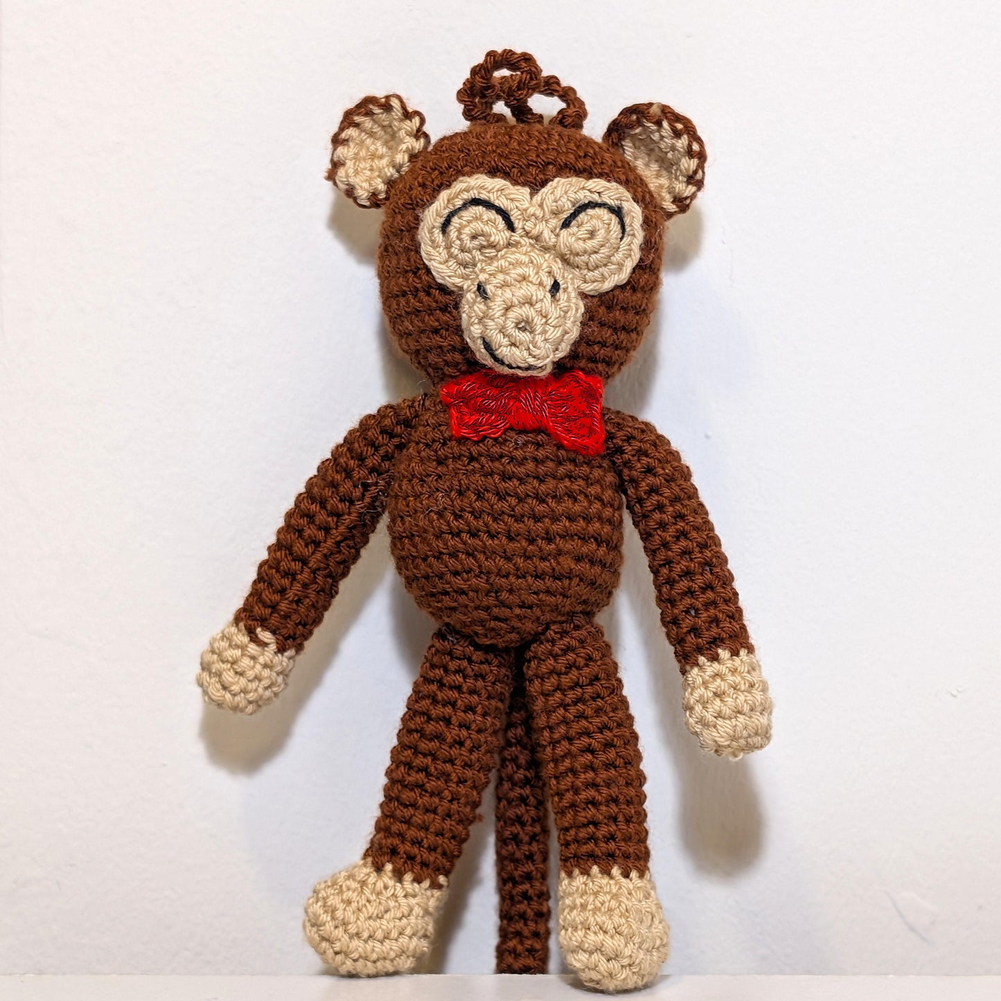 Standing crocheted chimpanzee wearing a red bow tie, attached to a string