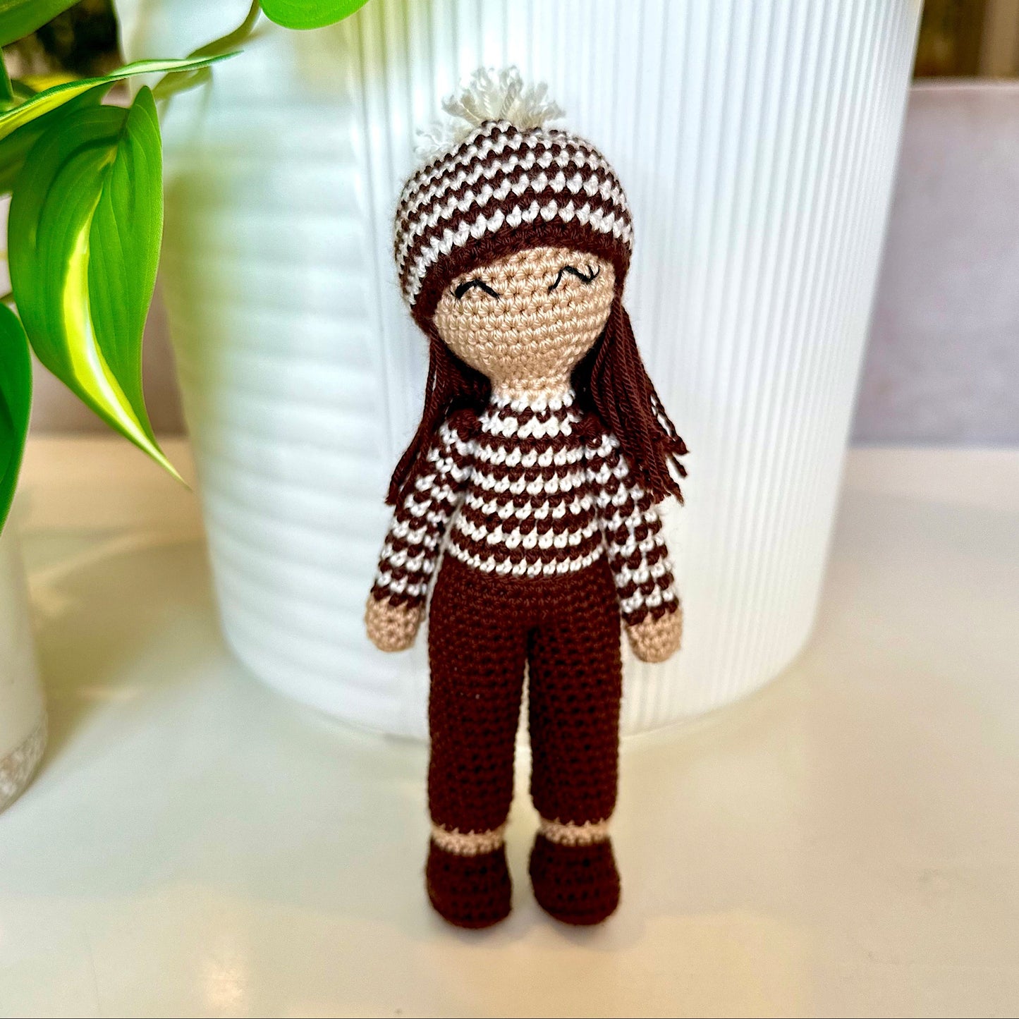 Crocheted amigurumi doll in striped shirt and hat and burnt maroon colored pants