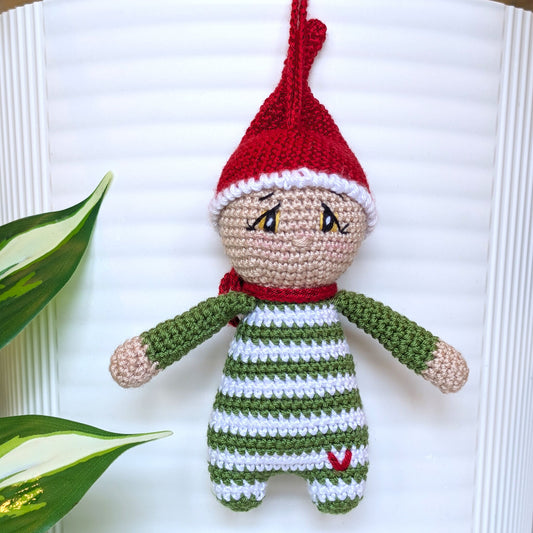 Crocheted elf with red hat and green and white striped outfit with a sweet worried look on a white background