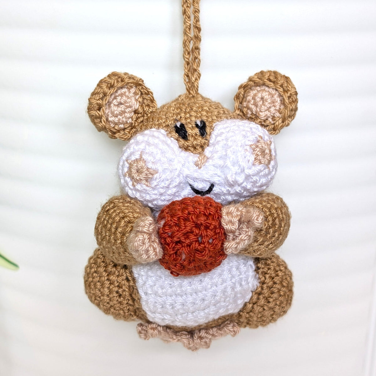 Crochet sand brown hamster bag charm with a string holding an terracotta colored ball
