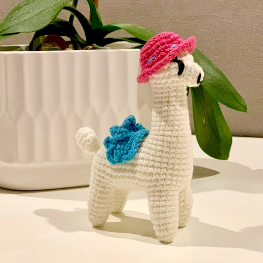 Crocheted plush llama toy with a pink hat and azure blue saddle.