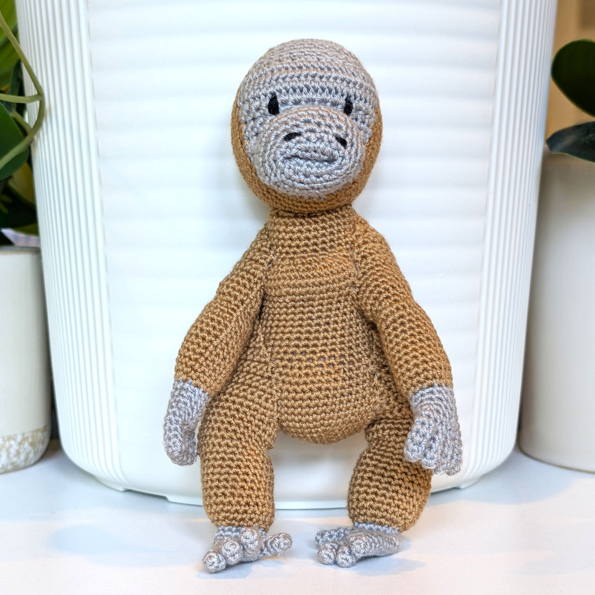 A crocheted plush toy orangutan sitting in front of a white ribbed planter