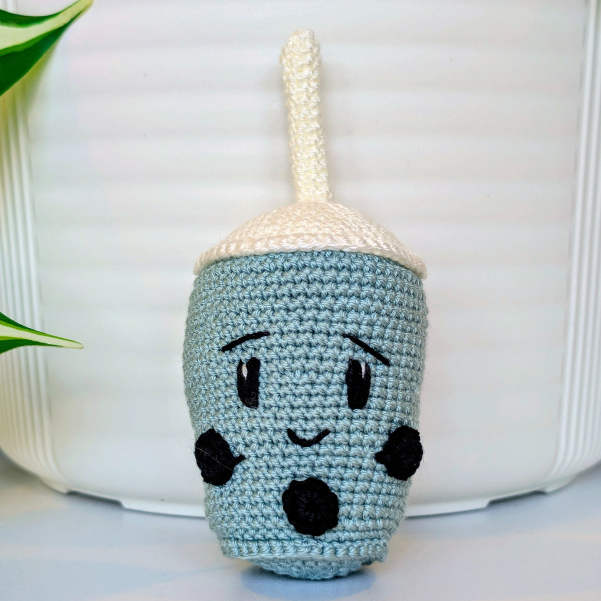 Crocheted seafoam boba tea cup with a face on a white background