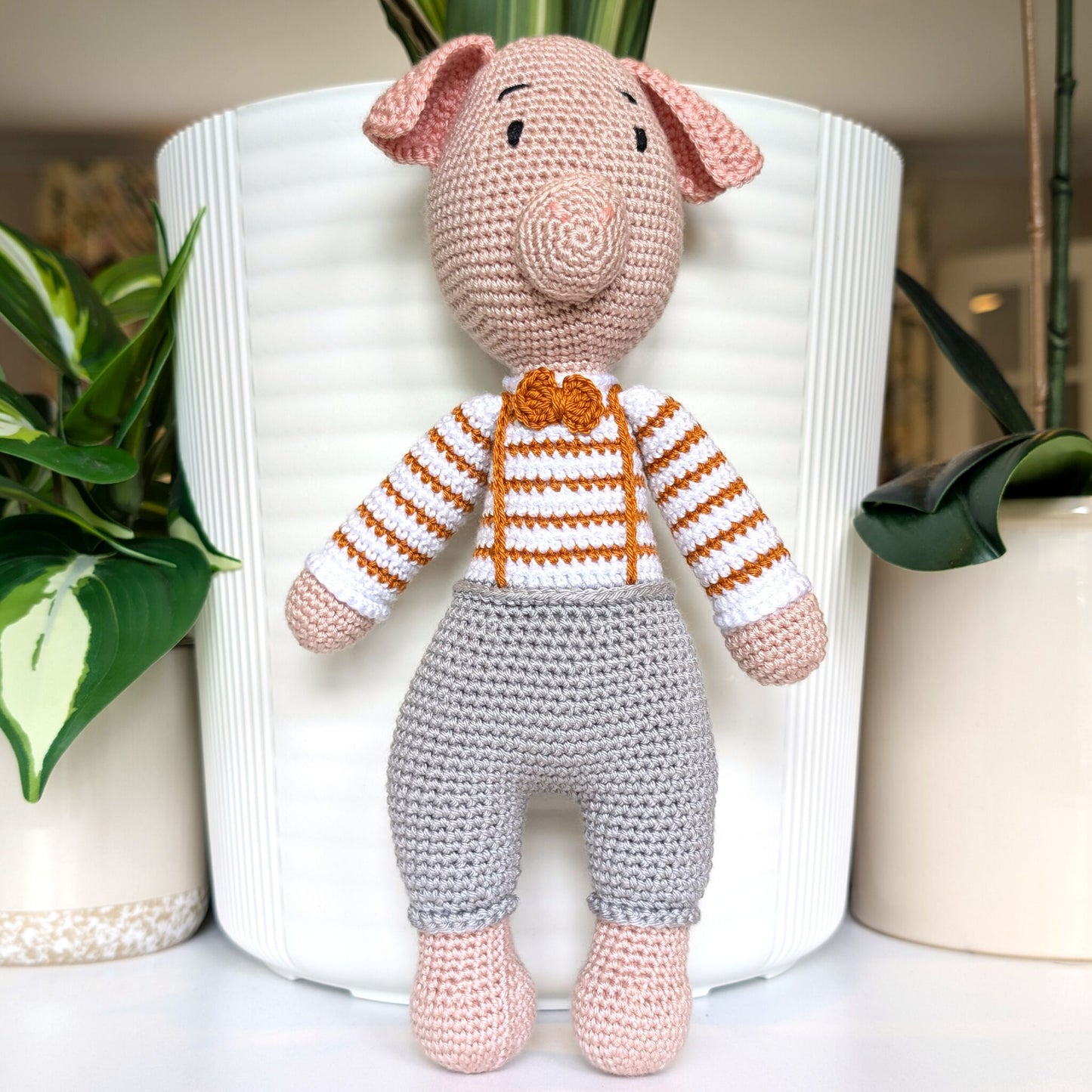 Crocheted standing pig wearing a striped ginger sweater, gray pants and a bow tie