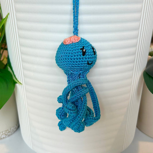 Right side profile of crocheted octopus charm in azure with a melon pink bow