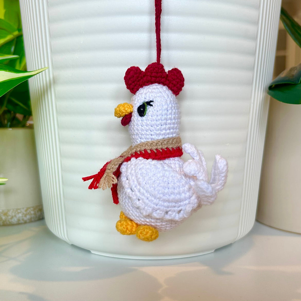 Right side profile of white crocheted chicken charm with a ruby red comb and a red and tan scarf
