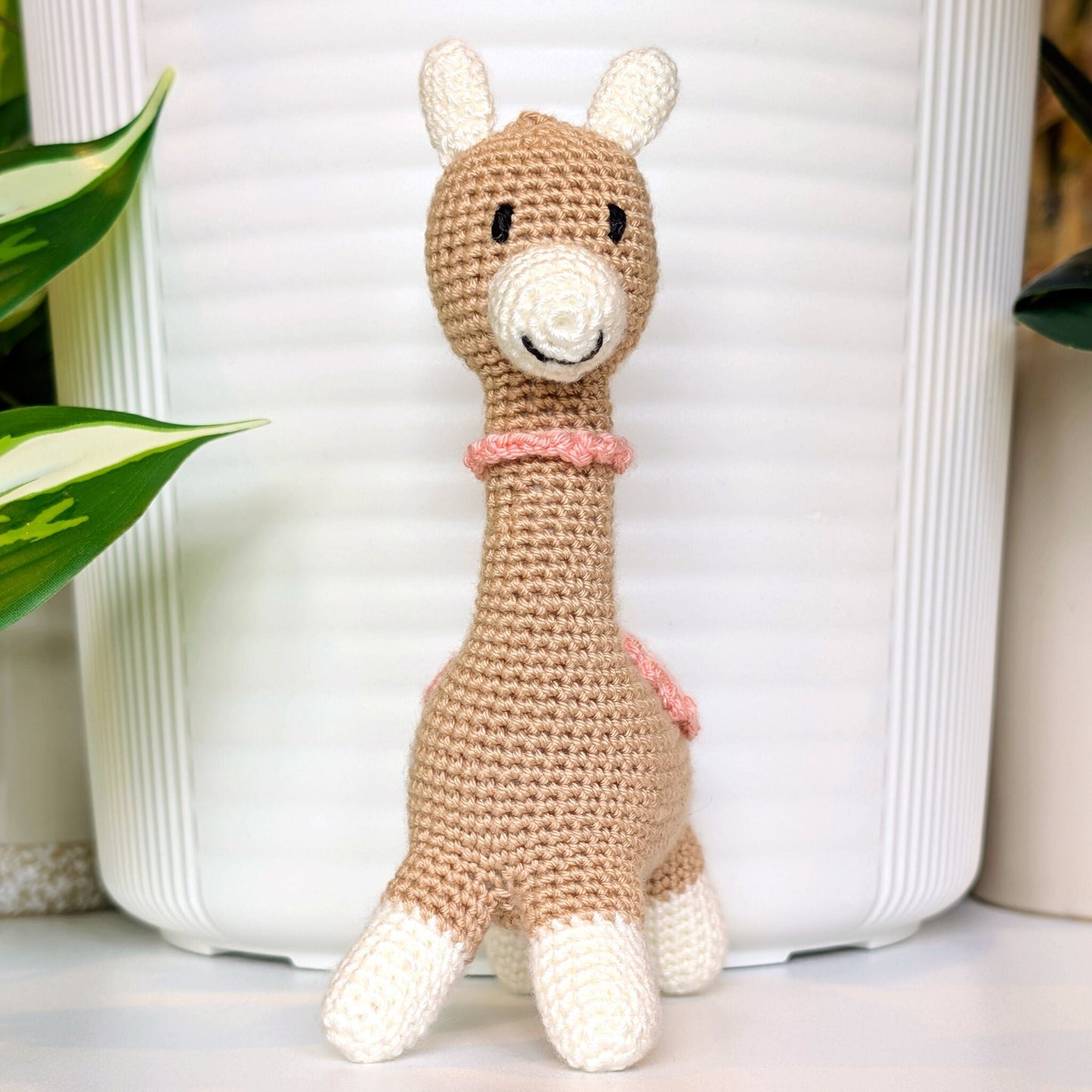Crocheted Vicuna llama plush with a necklace and pink, white saddle