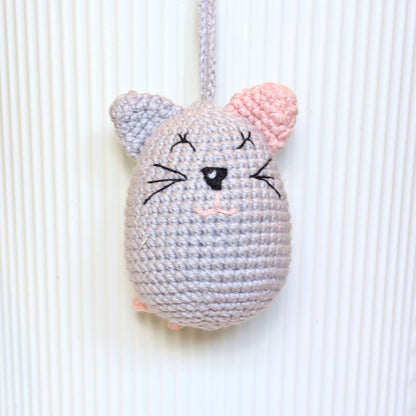 A crocheted mouse-shaped ornament or plush toy in light gray yarn with pink inner ears, embroidered black facial features, and a gray hanging loop at the top, shown against a white ribbed background.