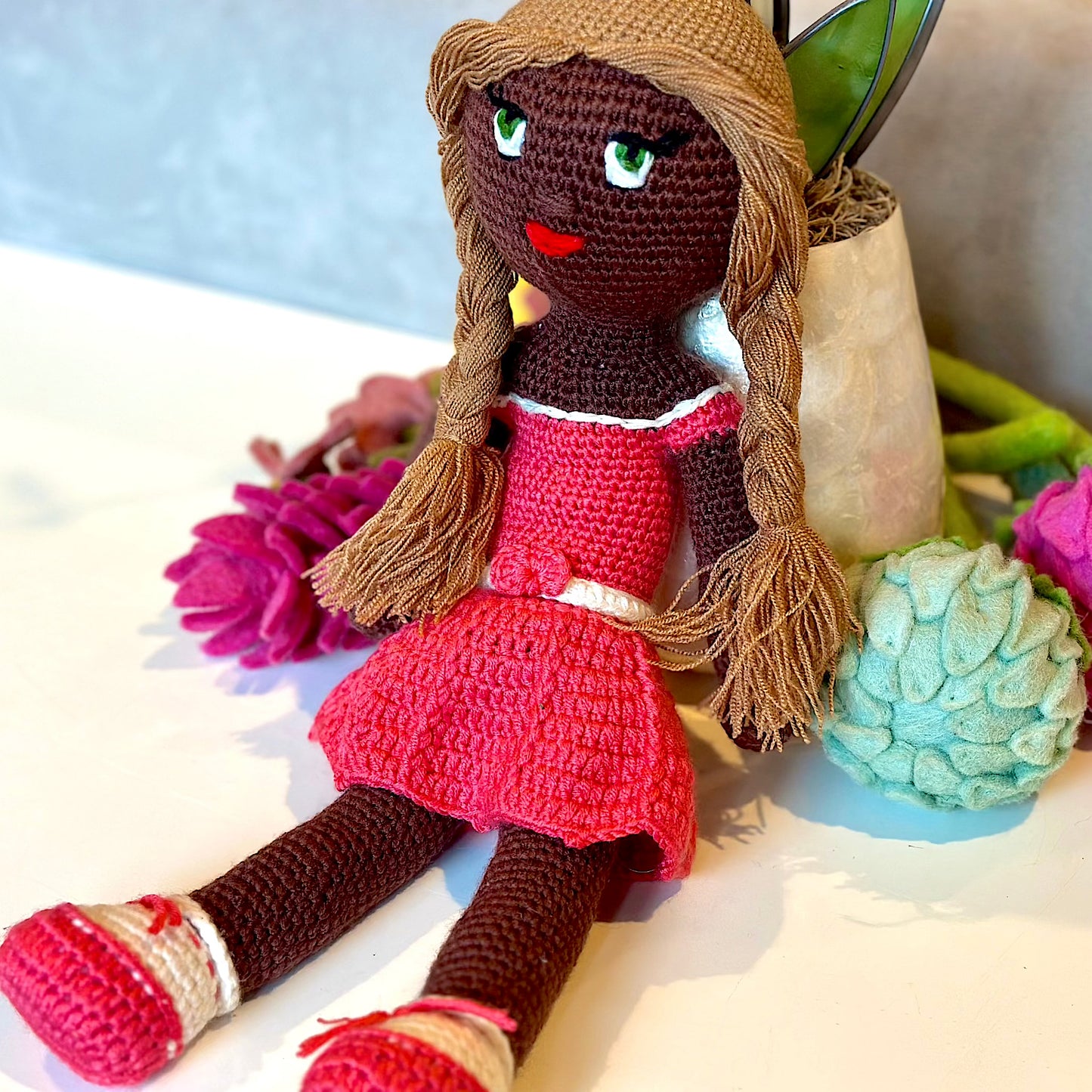 Crocheted plush black doll with golden brown hair in braids with a pink dress and shoes.