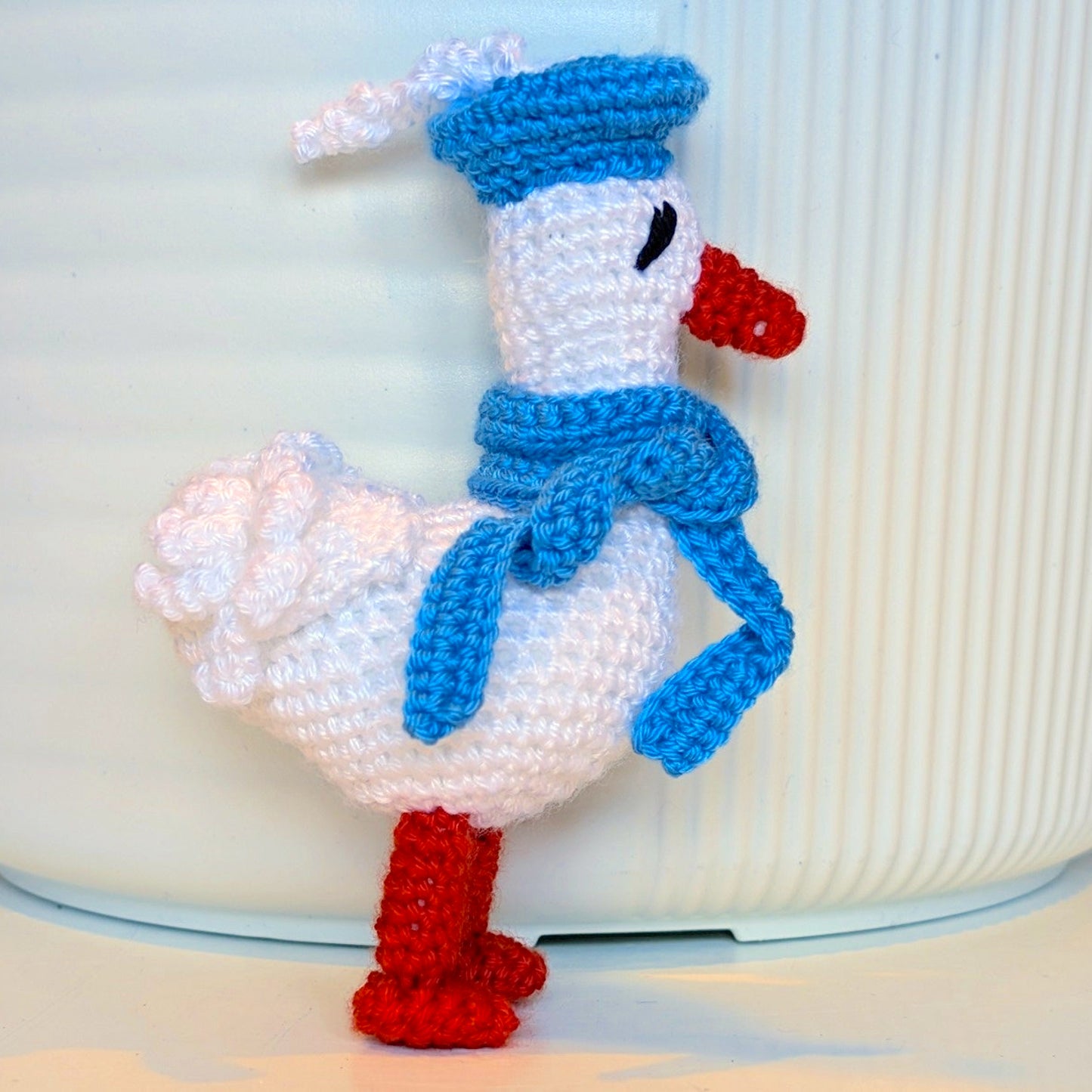 Crocheted duck keychain charm wearing an azure beret and scarf, attached to a string