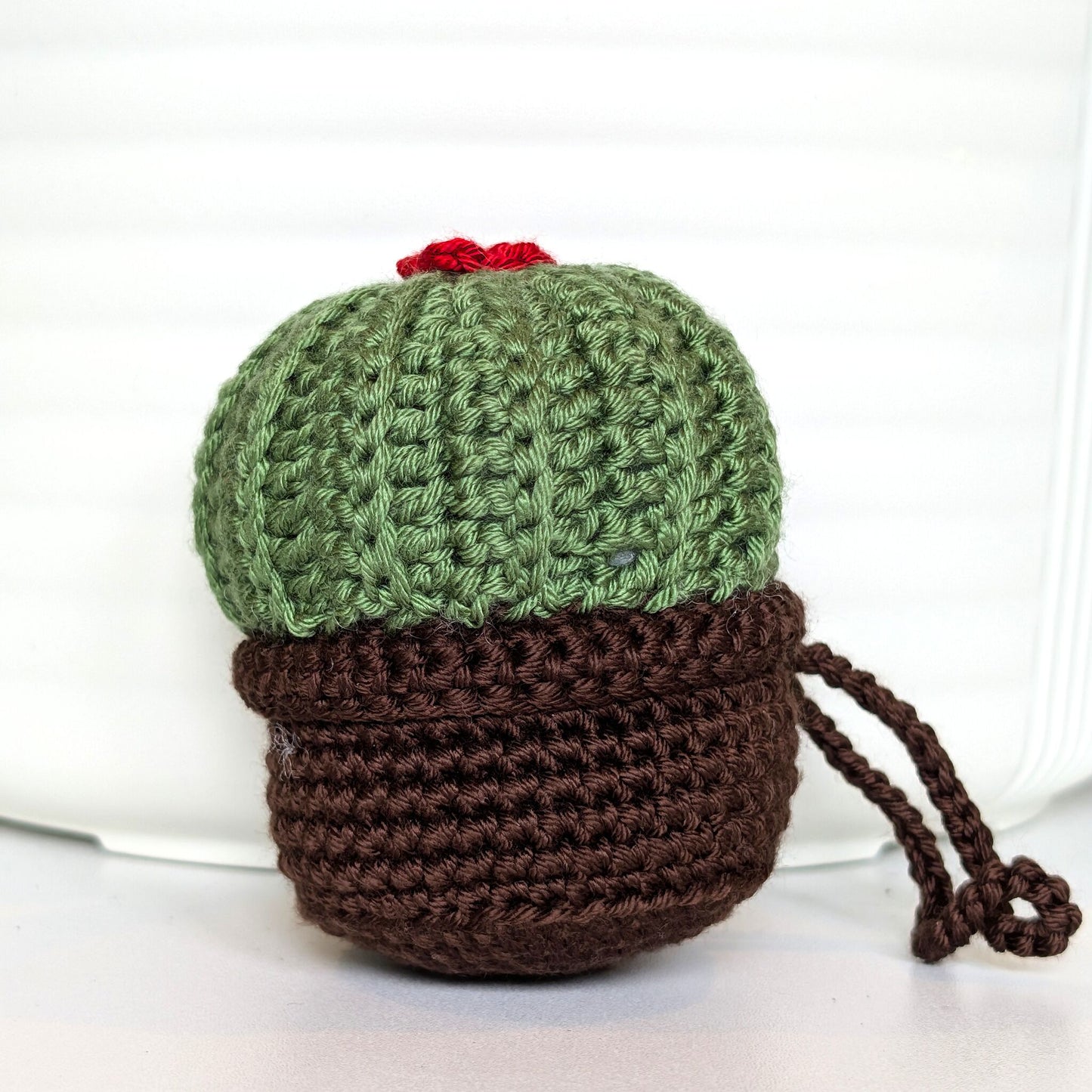 Crocheted moon cactus charm with a red flower and attached string, potted in a brown pot