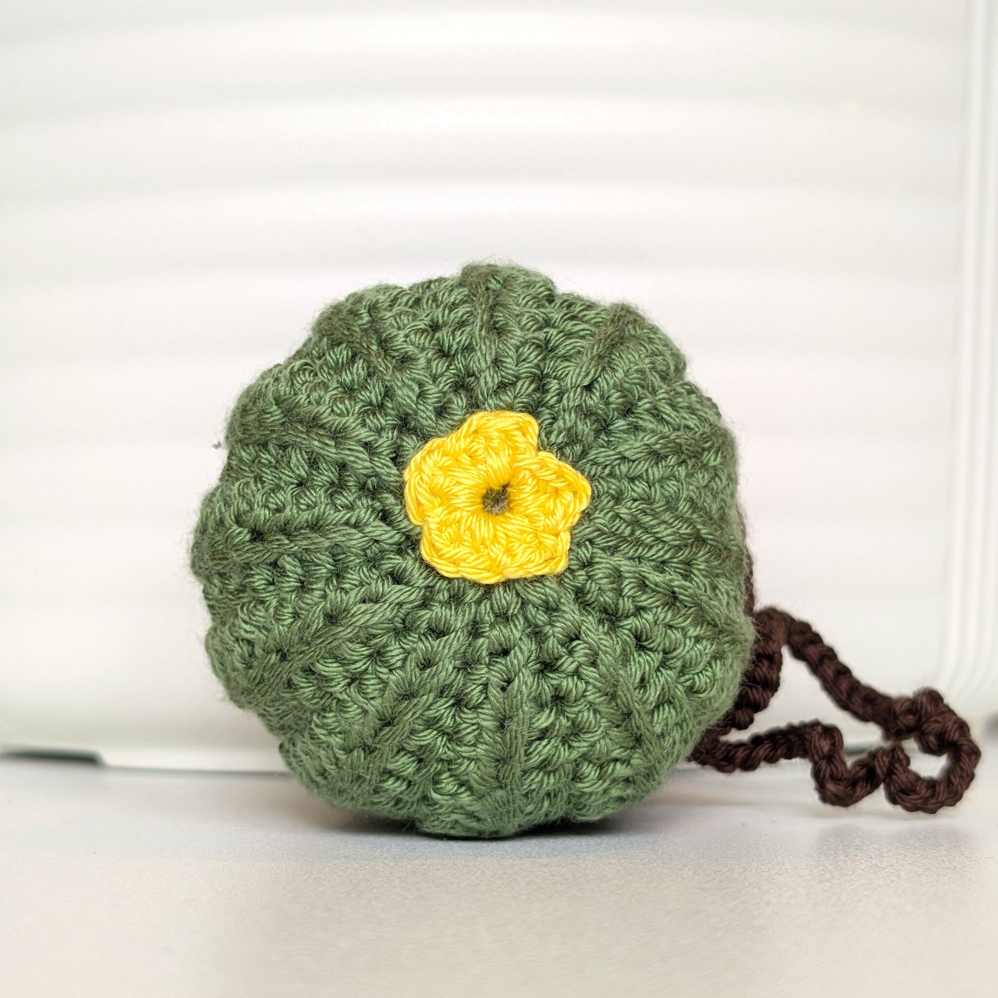 Tope view of crocheted moon cactus charm with a yellow flower and attached string, potted in a brown pot