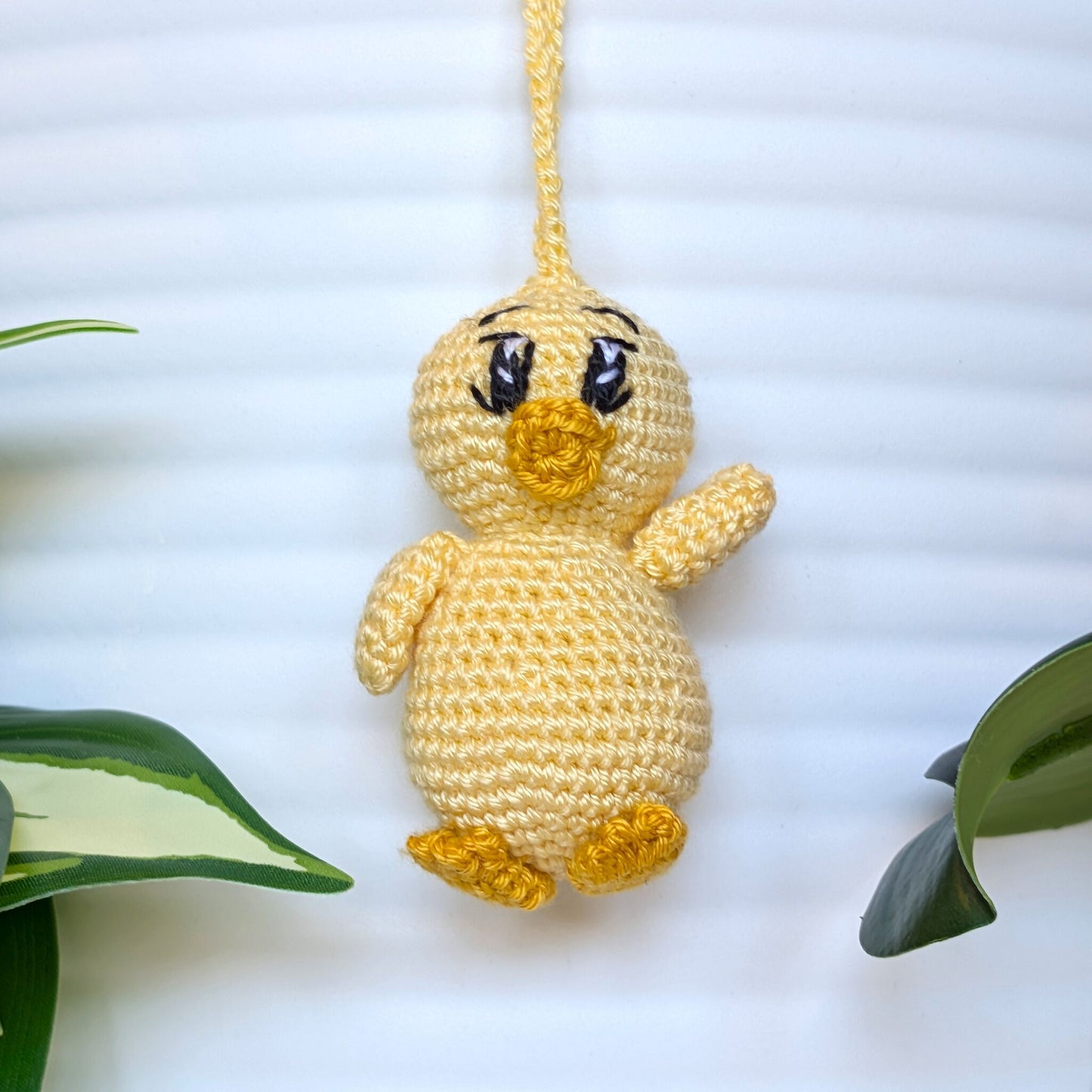 Crocheted light yellow chick with big sparkly eyes and a string