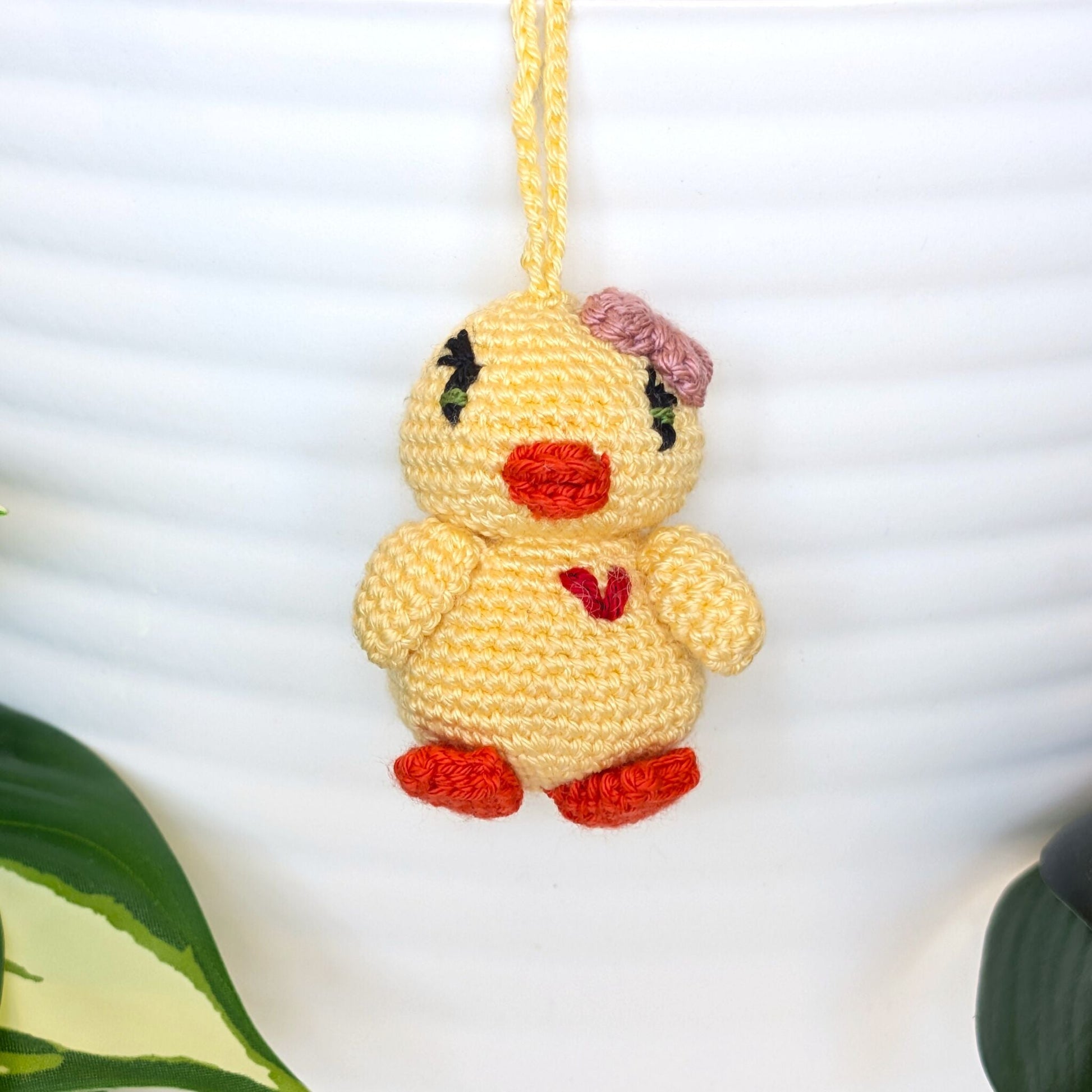 Crocheted yellow chick keychain with a pink bow, heart and a string