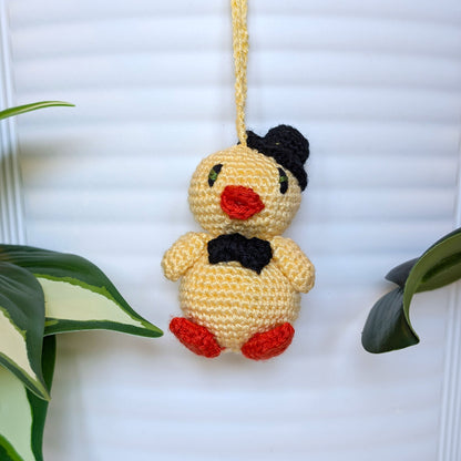 Crocheted light yellow chick with a hat, bow tie and a string