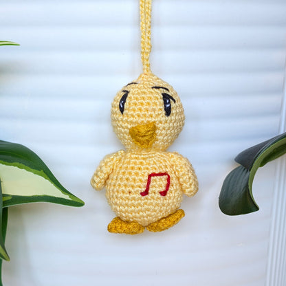 Crocheted light yellow chick with sparkly eyes, musical note and a string