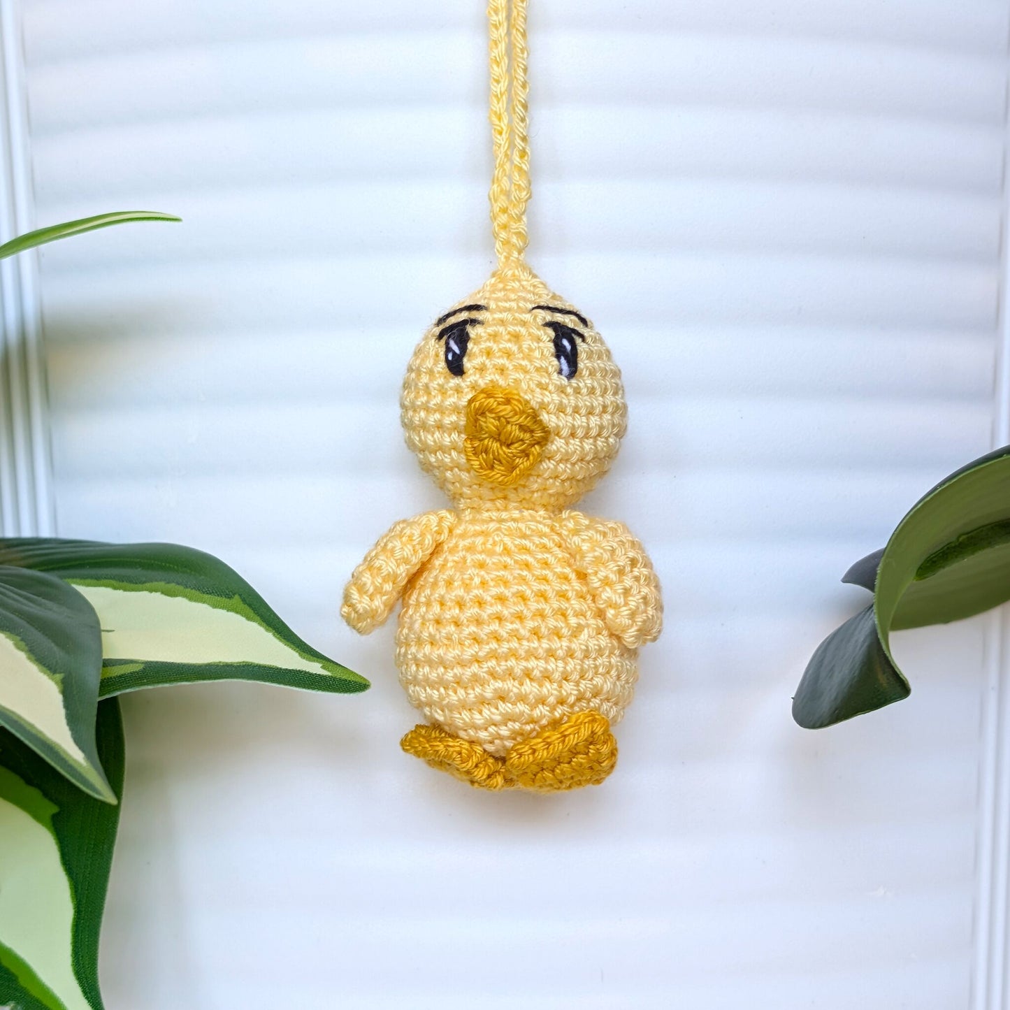 Crocheted light yellow chick with sparkly eyes and a string