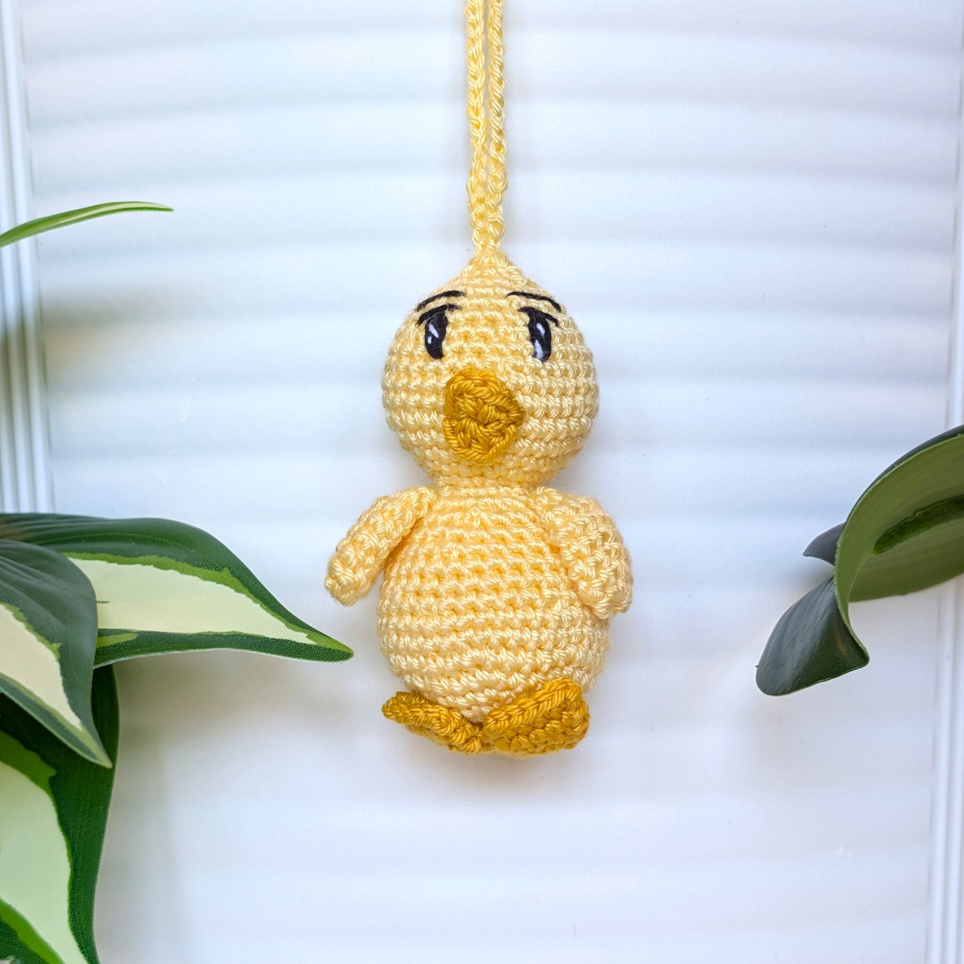 Crocheted light yellow chick with sparkly eyes and a string