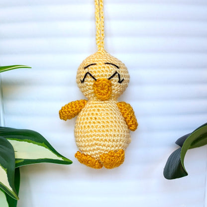 Crocheted light yellow chick with squinting eyes and a string