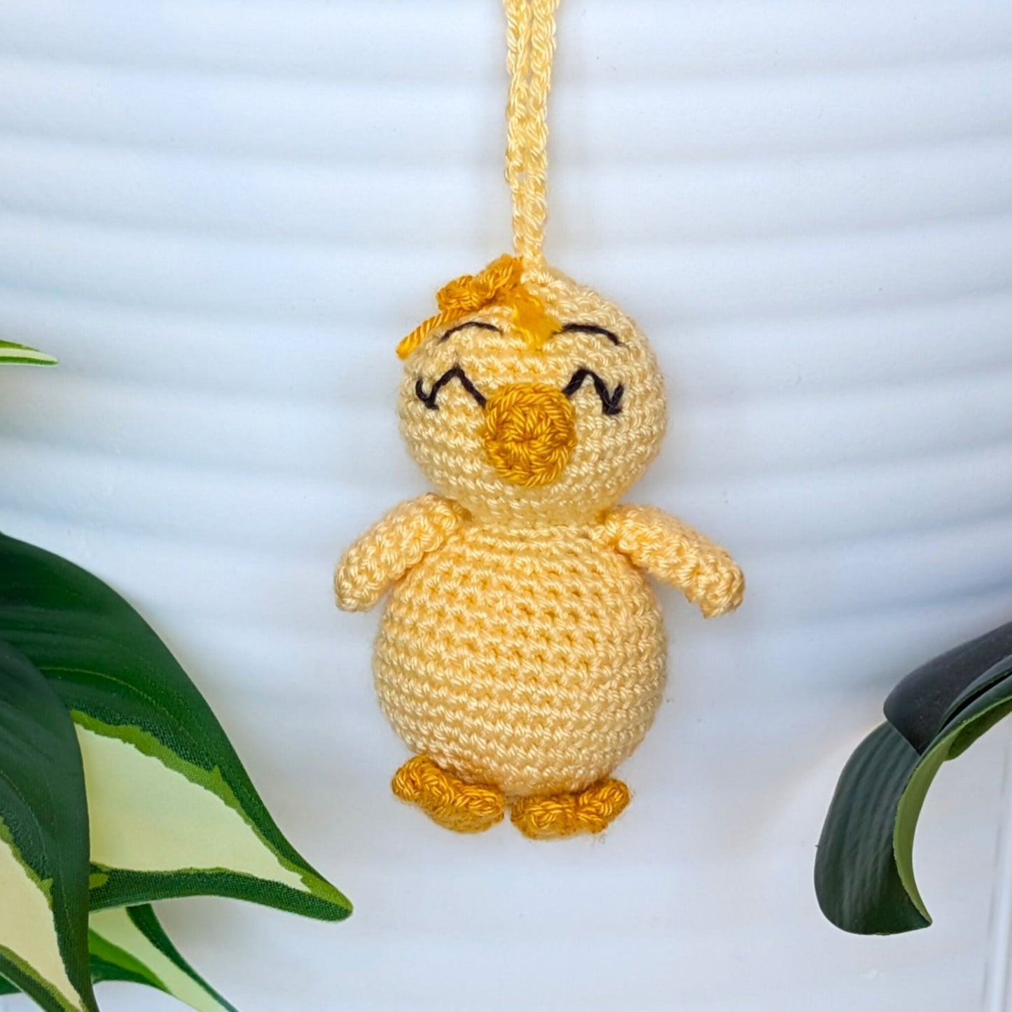 Crocheted light yellow chick with squinting eyes, bow and a string