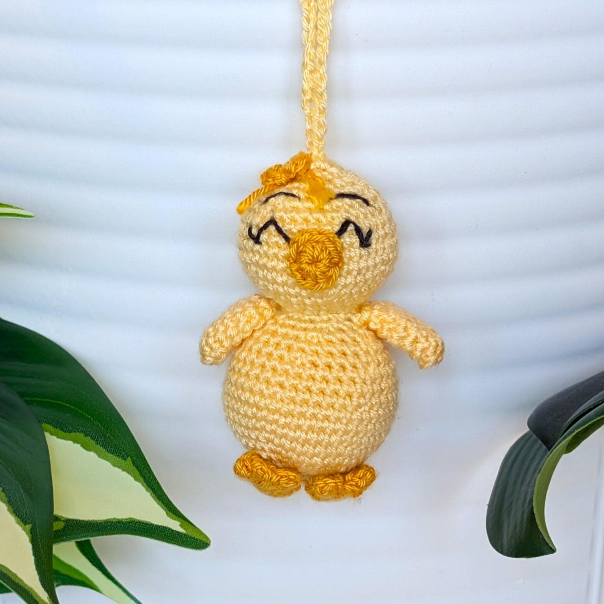 Crocheted light yellow chick with squinting eyes, bow and a string