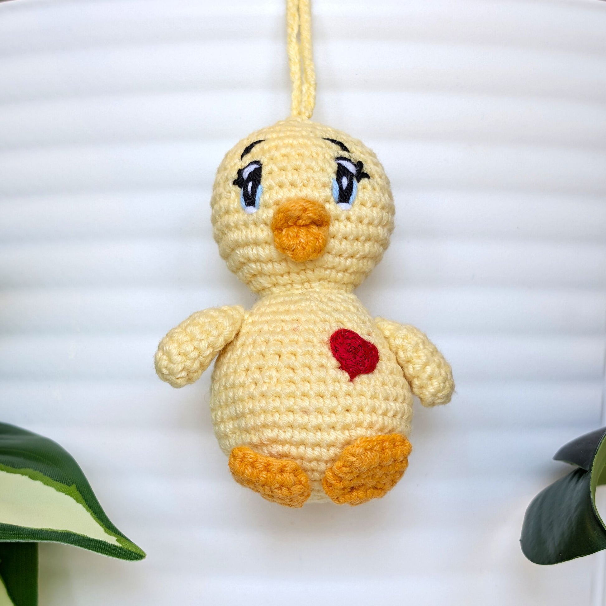 Crocheted light yellow chick with bluue sparkly eyes, heart and a string