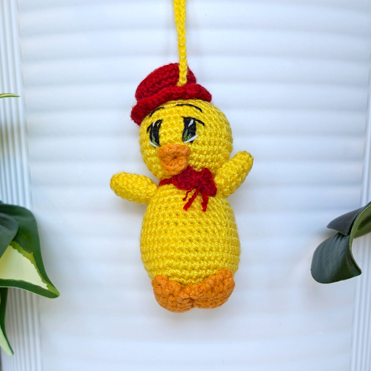 Crocheted yellow chick with green eyes and string wearing a hat