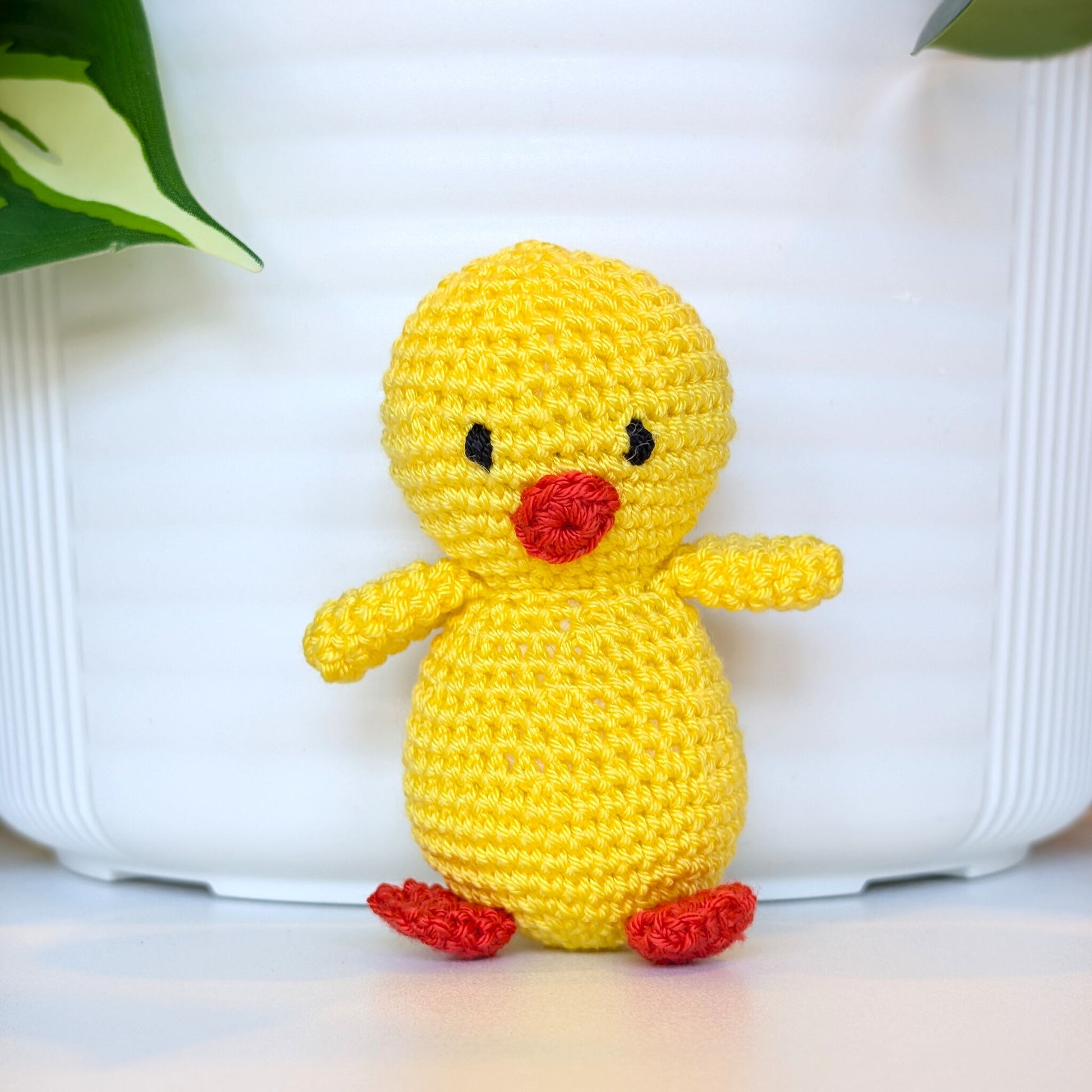 Crocheted yellow chick plush with standard black eyes, sitting on a white surface