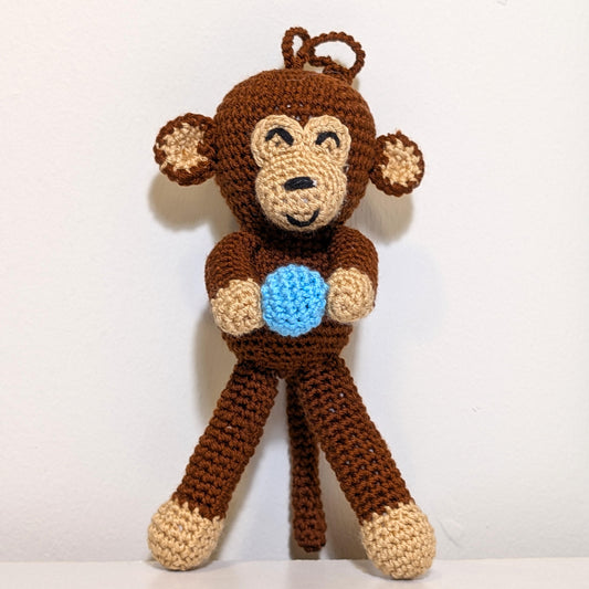 Brown crocheted standing chimpanzee holding a blue ball with a string