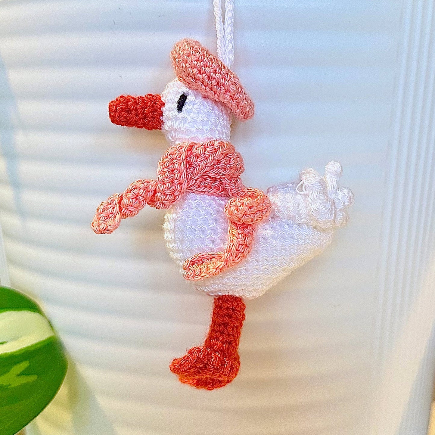 Crocheted duck keychain charm wearing a coral pink beret and scarf, attached to a string