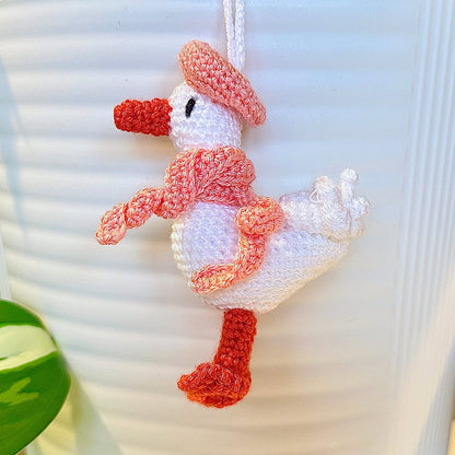 Crocheted duck keychain charm wearing a coral pink beret and scarf, attached to a string