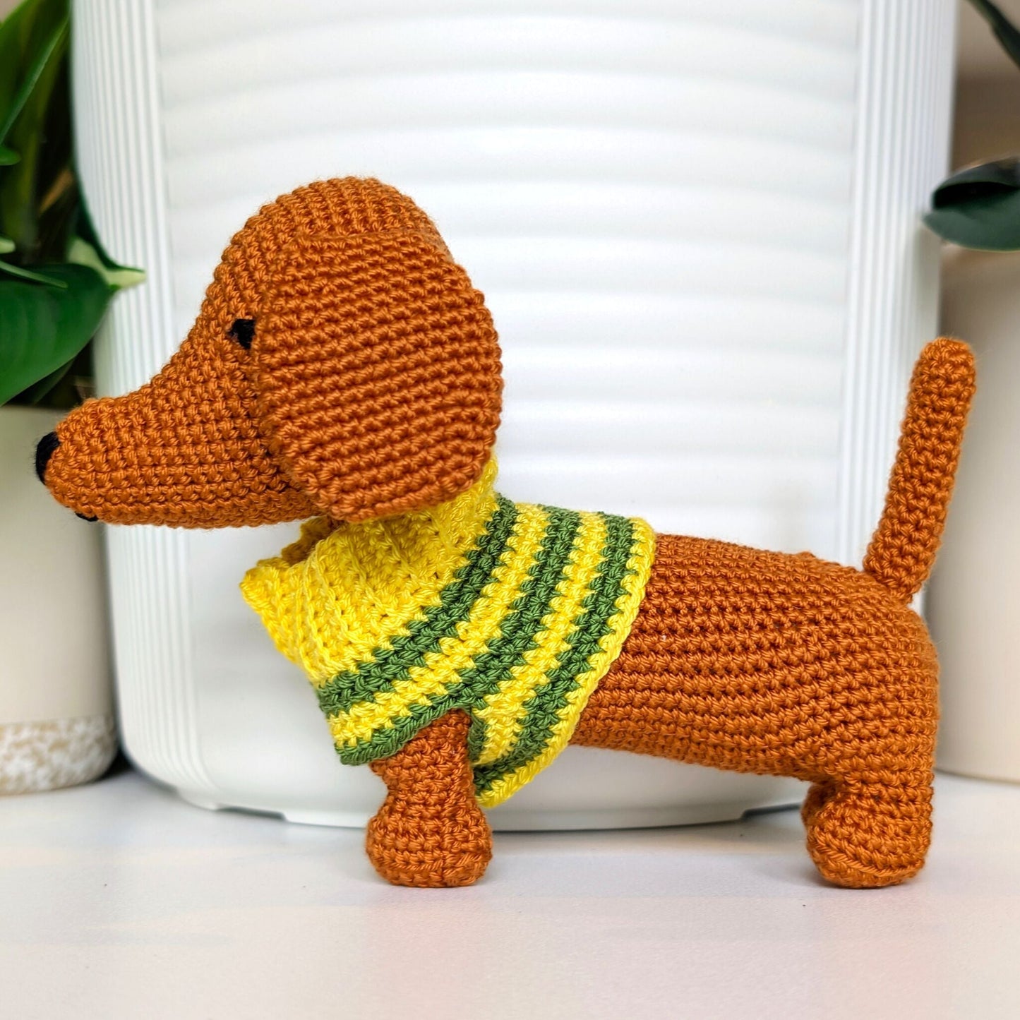Crocheted dachshund toy plush wearing a yellow and green striped sweater