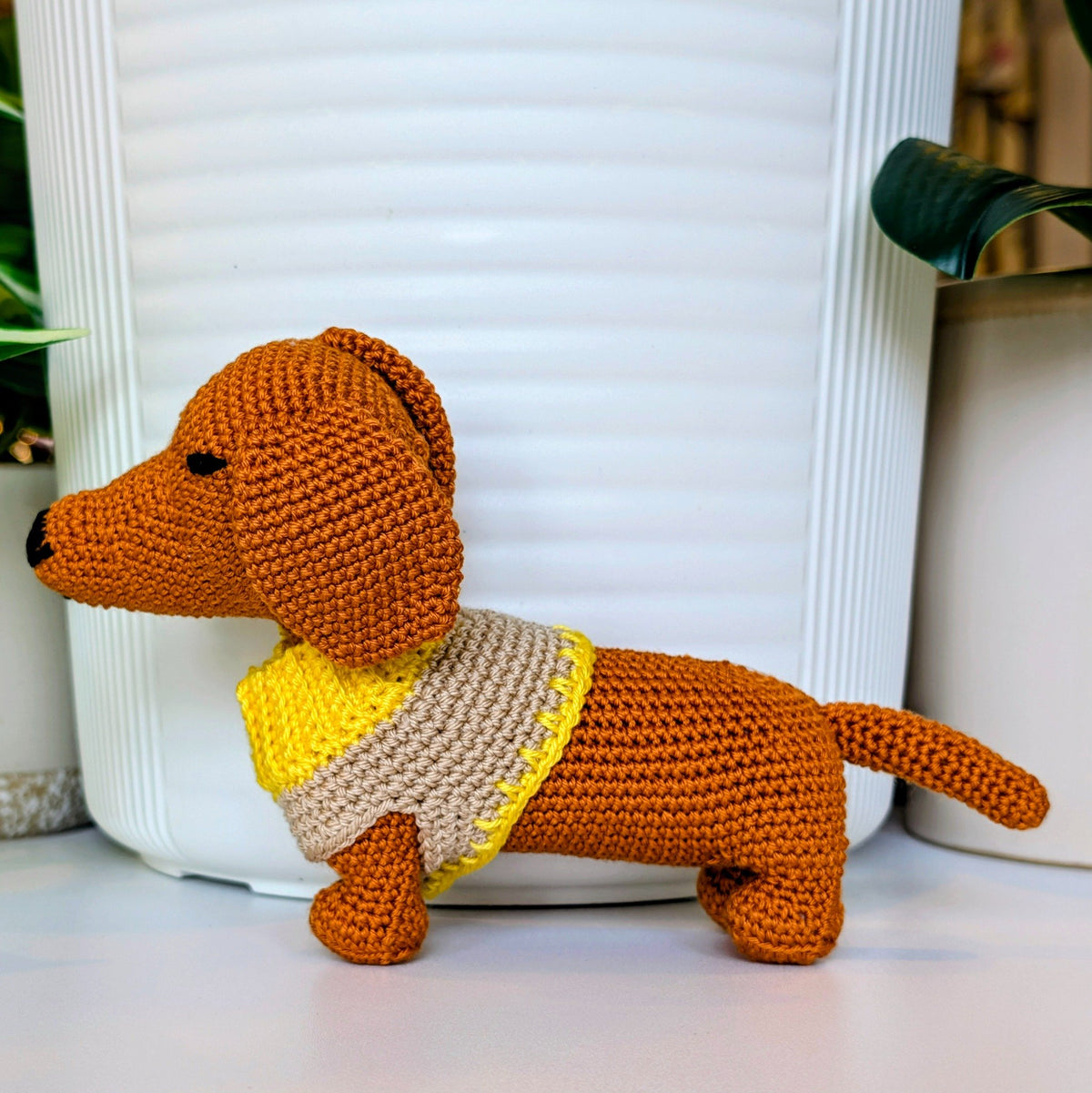 Crocheted dachshund dog wearing a sweater with a white background