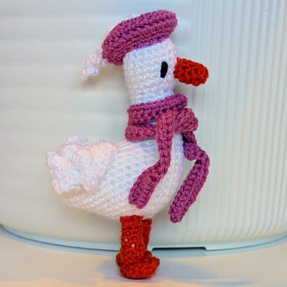 Crocheted duck keychain charm wearing a soft tulip colored beret and scarf, attached to a string