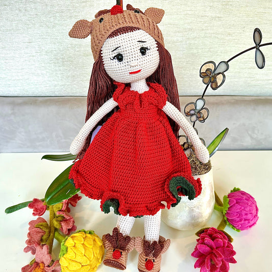 Crocheted doll with a red dress and reindeer hat surrounded by flowers on a white background
