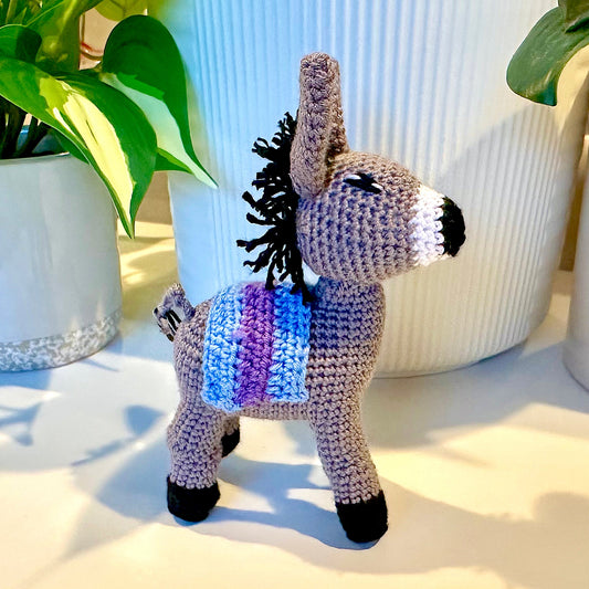 Amigurumi plush donkey  figurine with a crocheted saddle in sky blue and purple colors. 