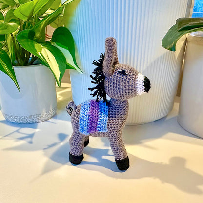 Crochet plush donkey toy in gray with sky blue and purple colored saddle
