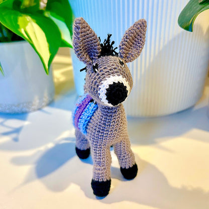 Crocheted plush donkey toy with a sky blue and purple colored saddle