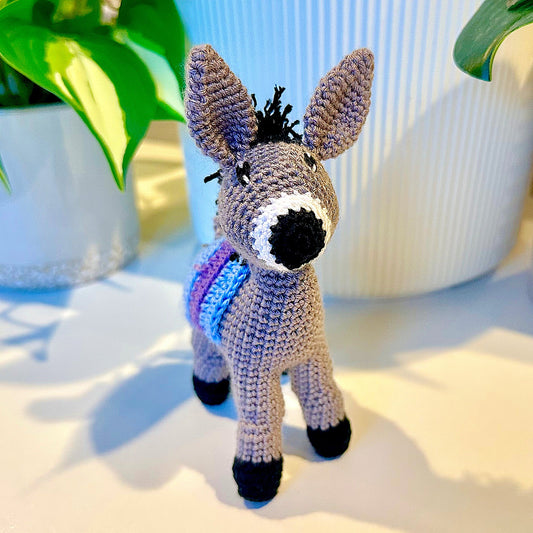 Crocheted plush donkey toy with a sky blue and purple colored saddle