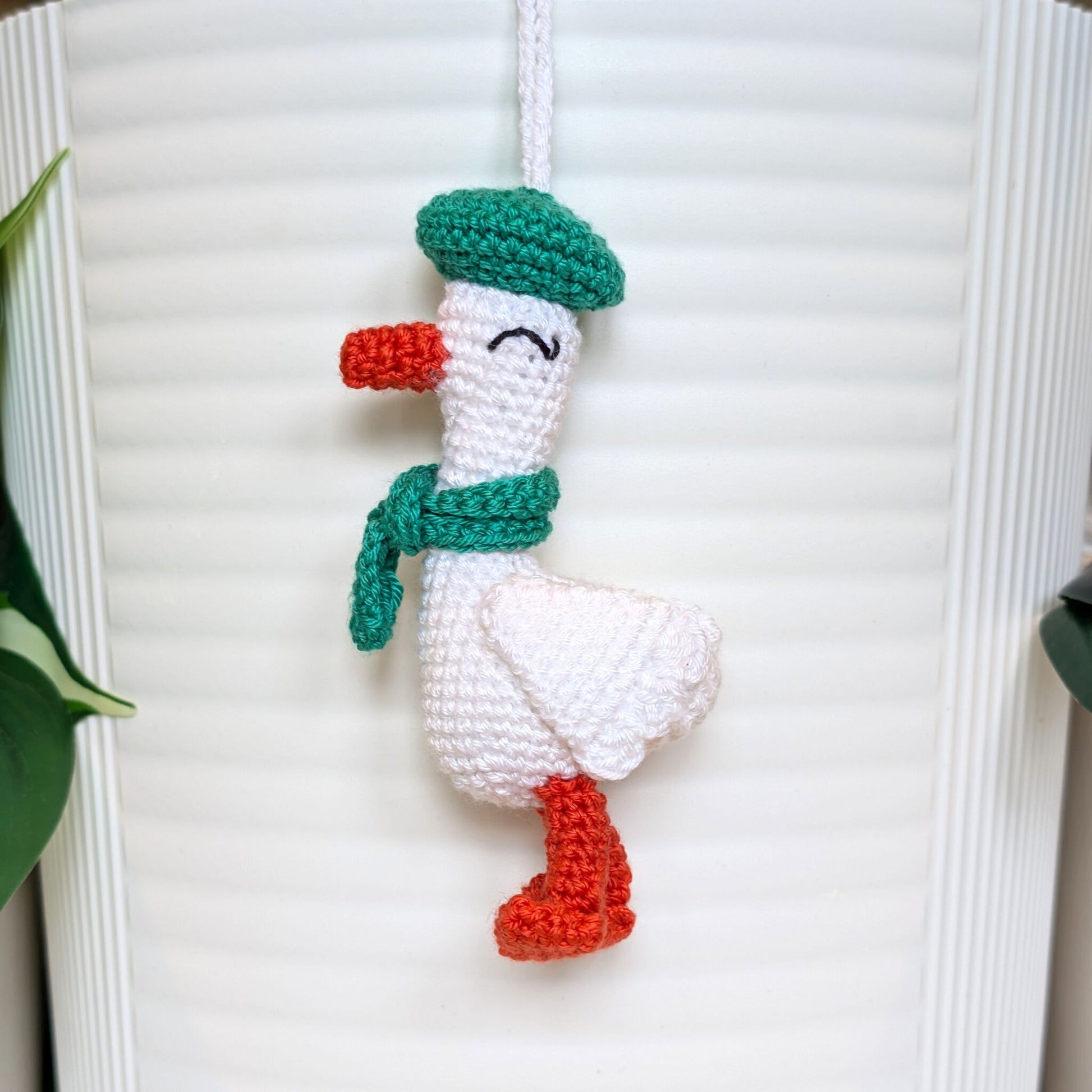 Crocheted duck keychain charm wearing an emerald green beret and scarf, attached to a string