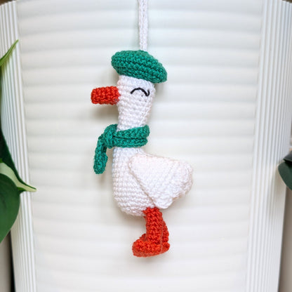 Crocheted duck keychain charm wearing an emerald green beret and scarf, attached to a string