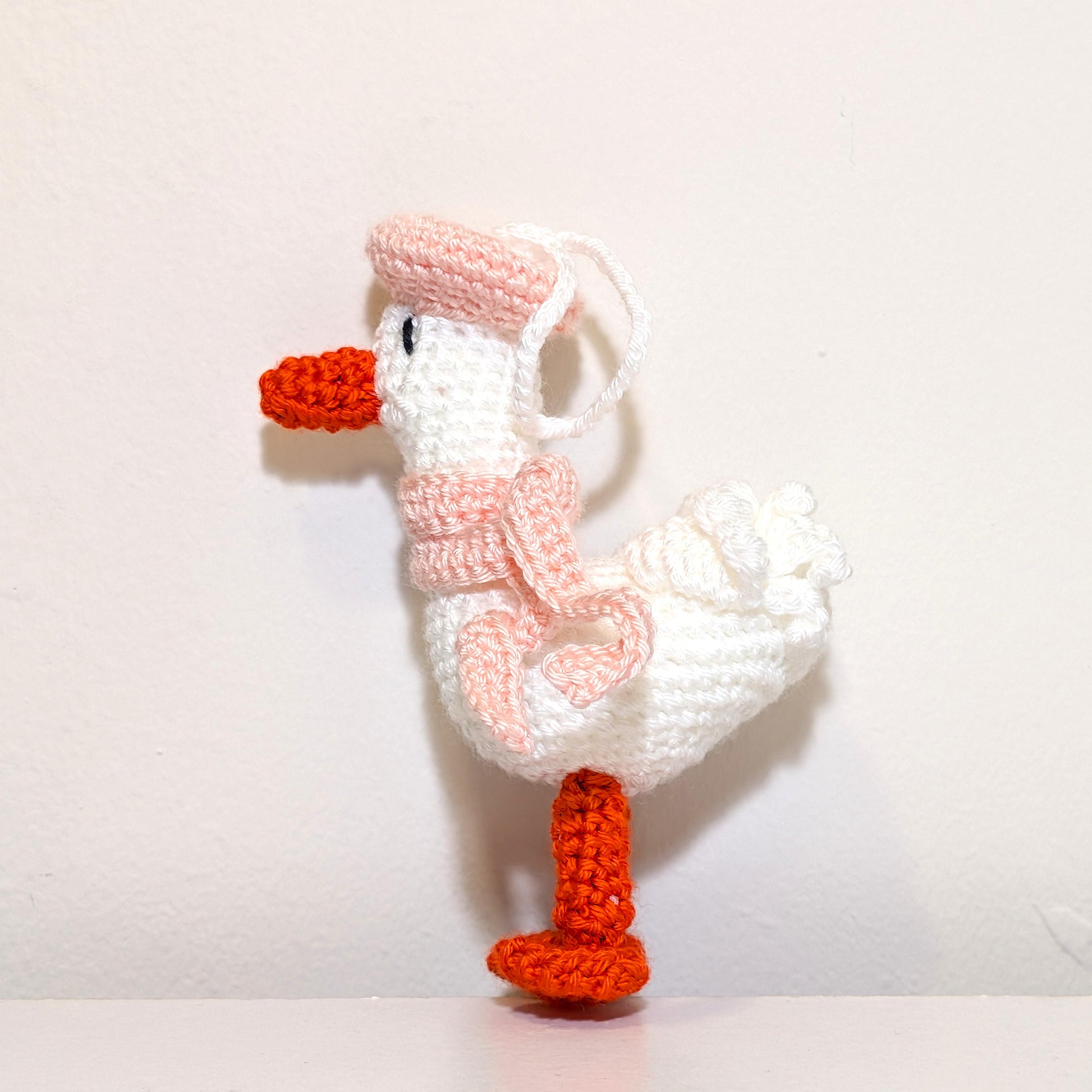 Crocheted duck keychain charm wearing a light pink beret and scarf, attached to a string