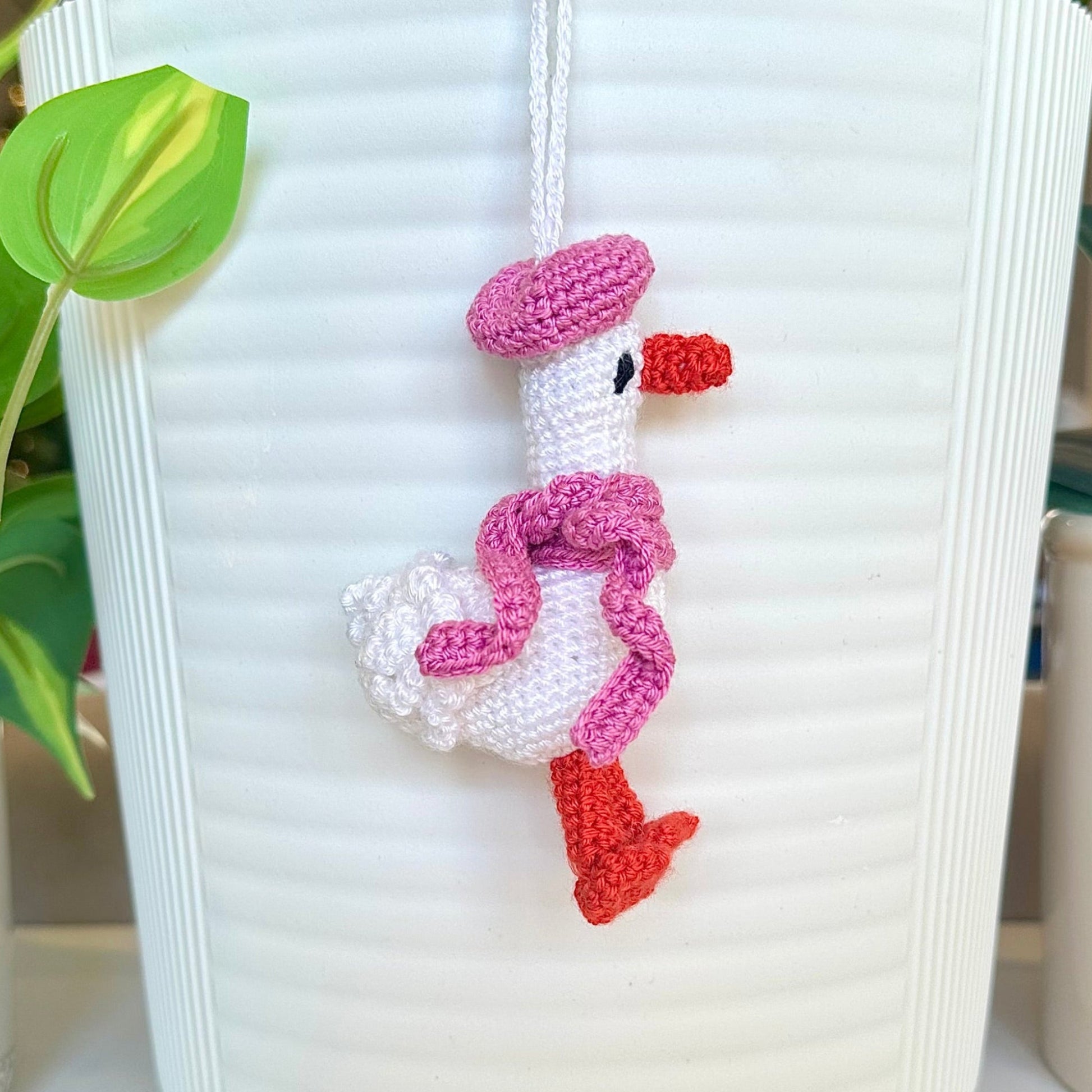 Crocheted duck keychain charm wearing an orchid colored beret and scarf, attached to a string