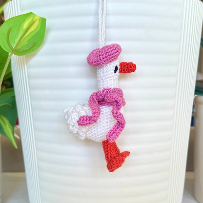 Crocheted duck keychain charm wearing an orchid colored beret and scarf, attached to a string