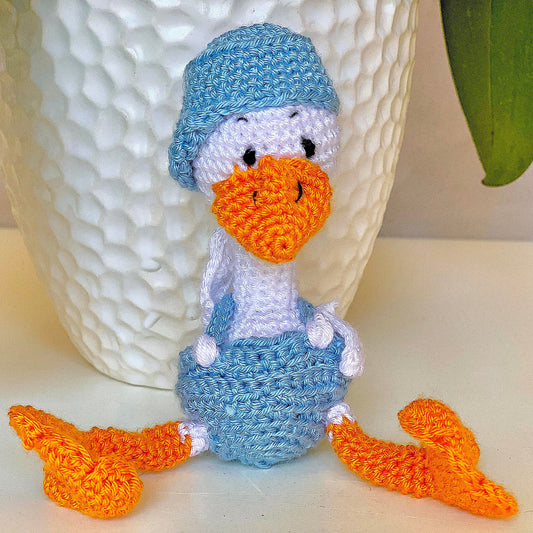 Crocheted plush duck toy with light blue suspenders and cap. 