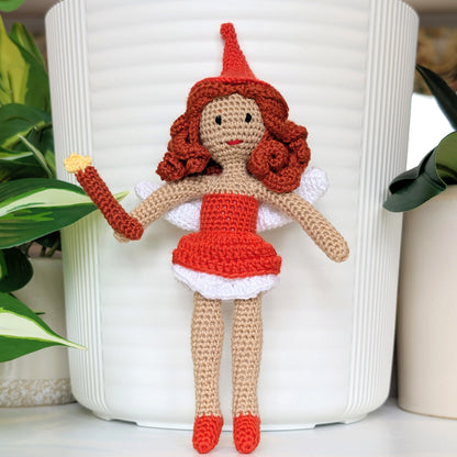 Crocheted fairy doll with red hair and bright orange dress and a hat, holding a wand