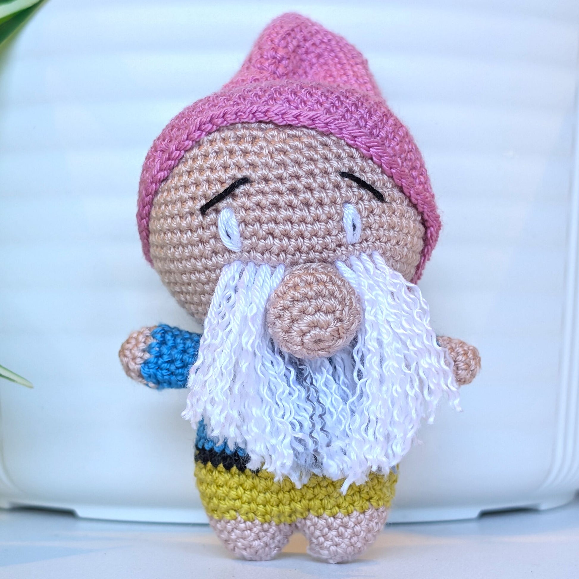 Crocheted plush gnome toy with a pink hat and white beard on a light background