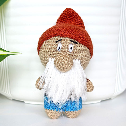 Handmade crocheted gnome figurine toy with happy expression, white beard, mahogany colored hat and brilliant azure blue pants